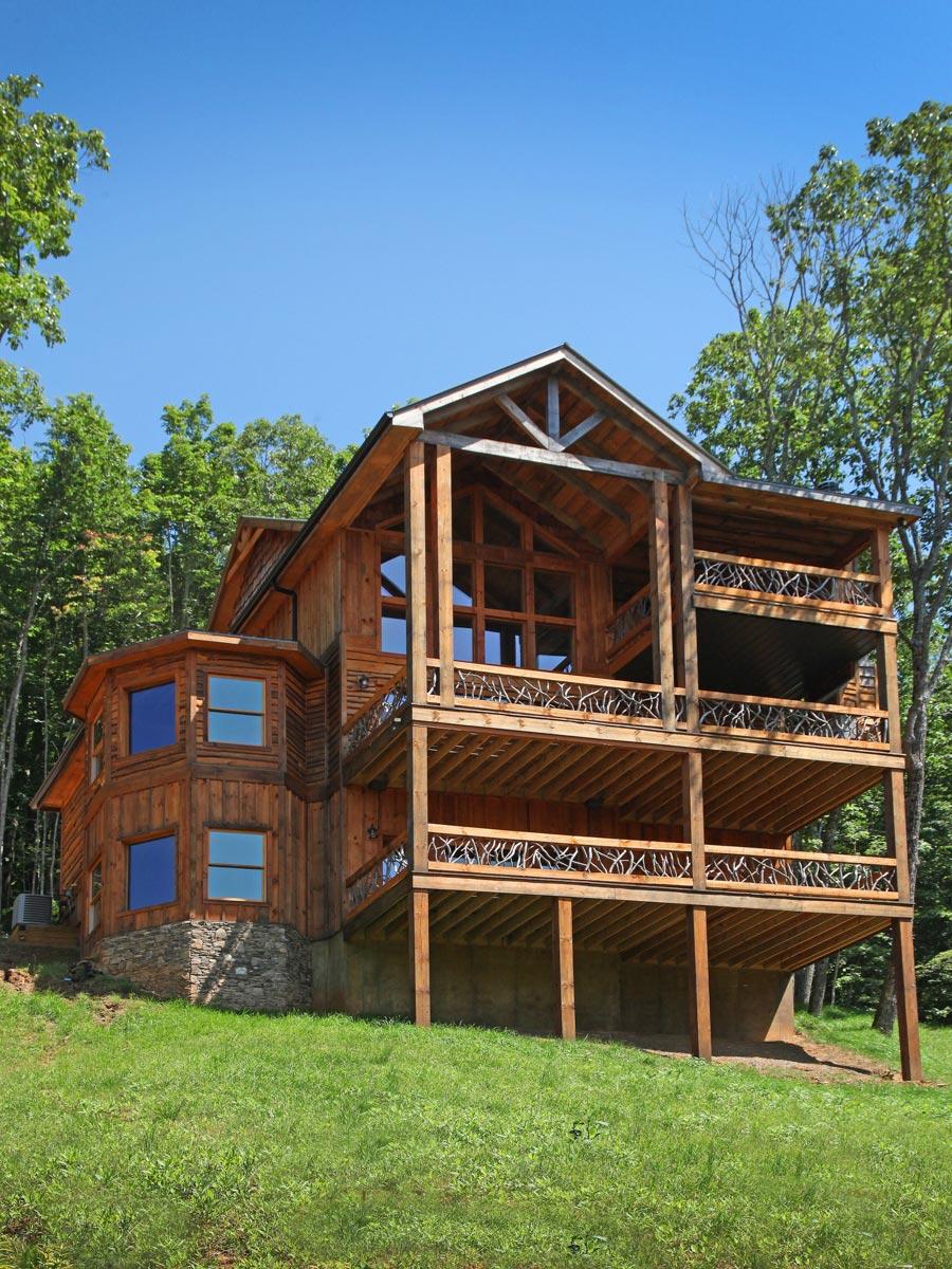 Log house exterior with multi-level decks, stone foundation, and prominent wooden beam gable.