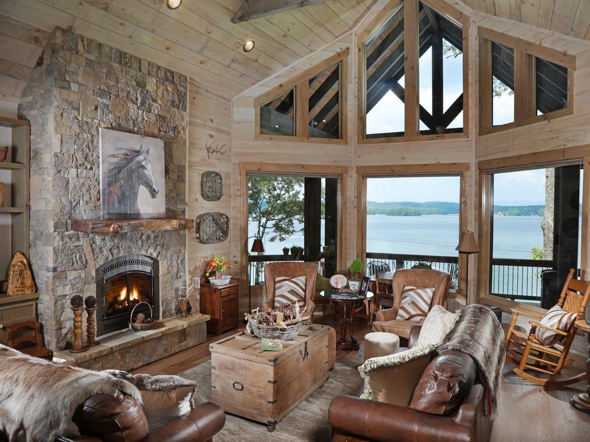 Great room with stone fireplace, wood-paneled walls, vaulted ceiling with triangular windows, and lake view.