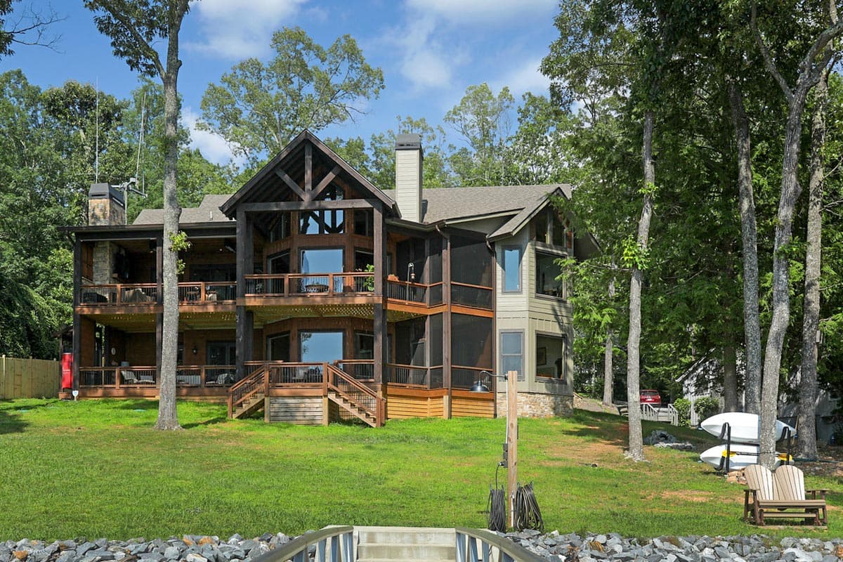 Lake house plan exterior with multiple levels of decking, stone chimney, and large windows.