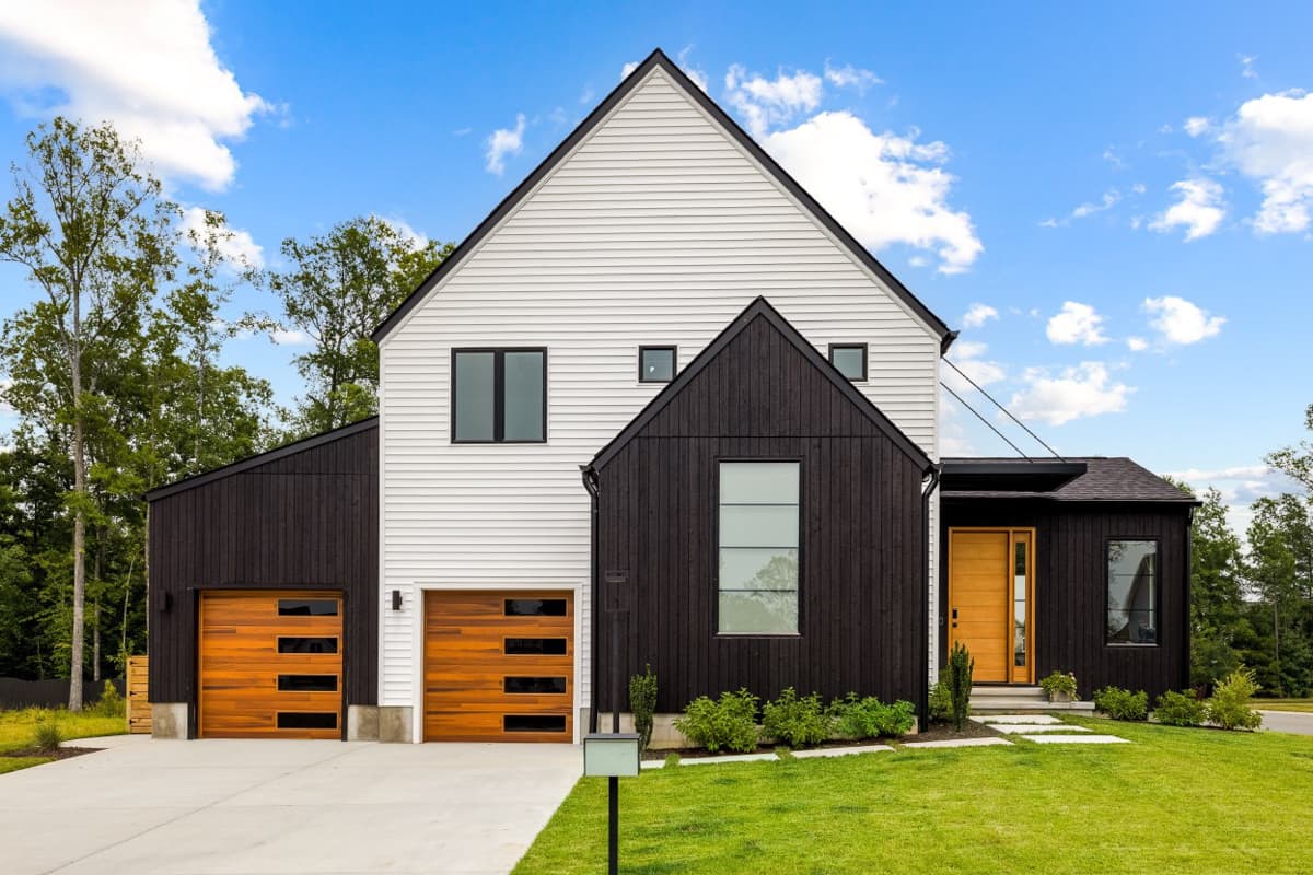 House plan exterior. Modern Farmhouse style with two stories, two-car garage, multiple gables, and contrasting dark and white siding.