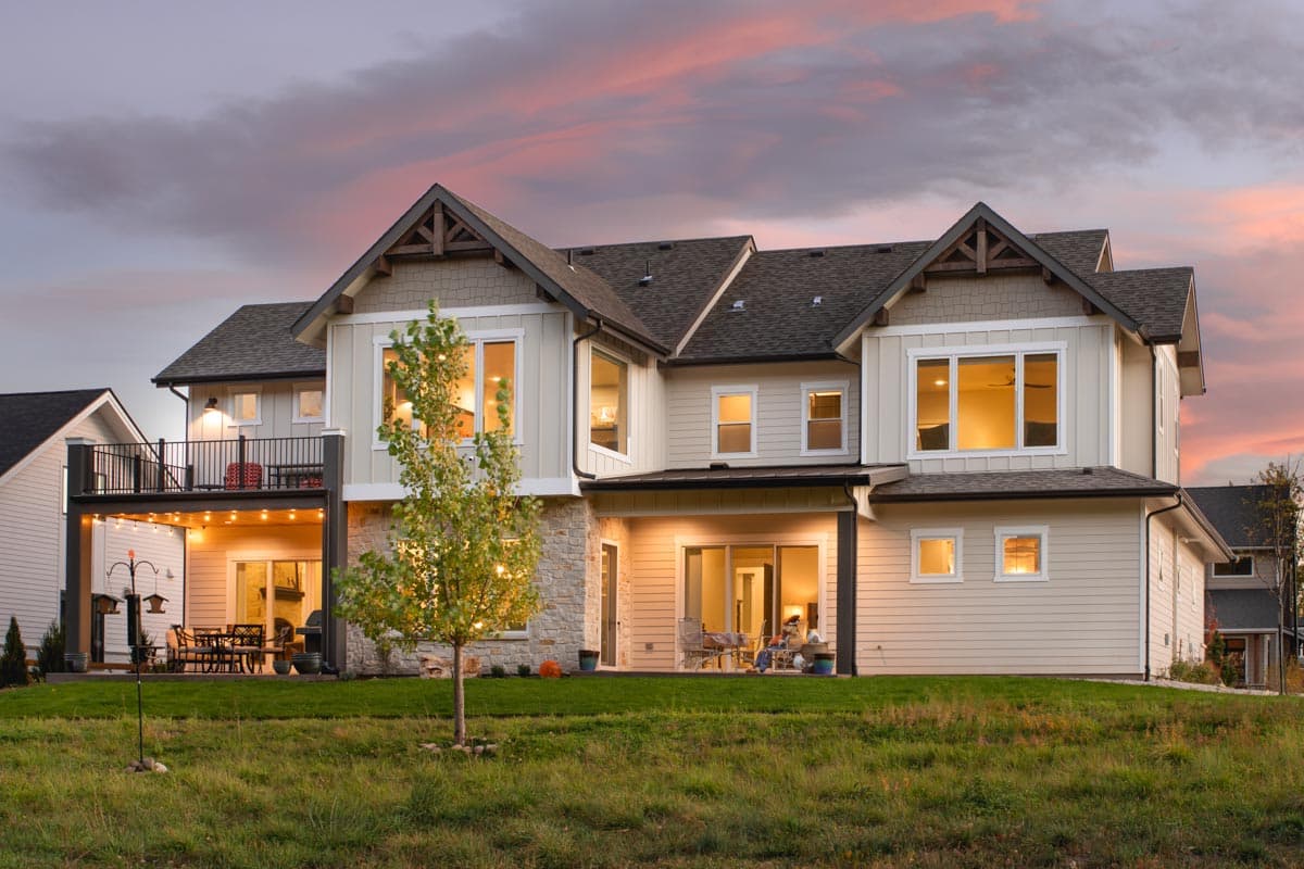Two-story house plan exterior with multiple gables, stone accents, a second-story balcony, and covered patio with outdoor lighting.