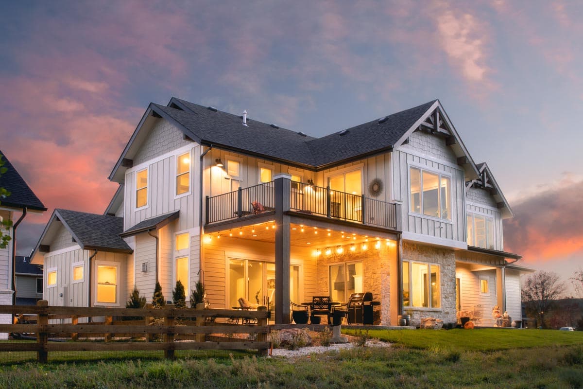 Two-story house plan exterior with a balcony, covered patio with string lights, and stone accents.