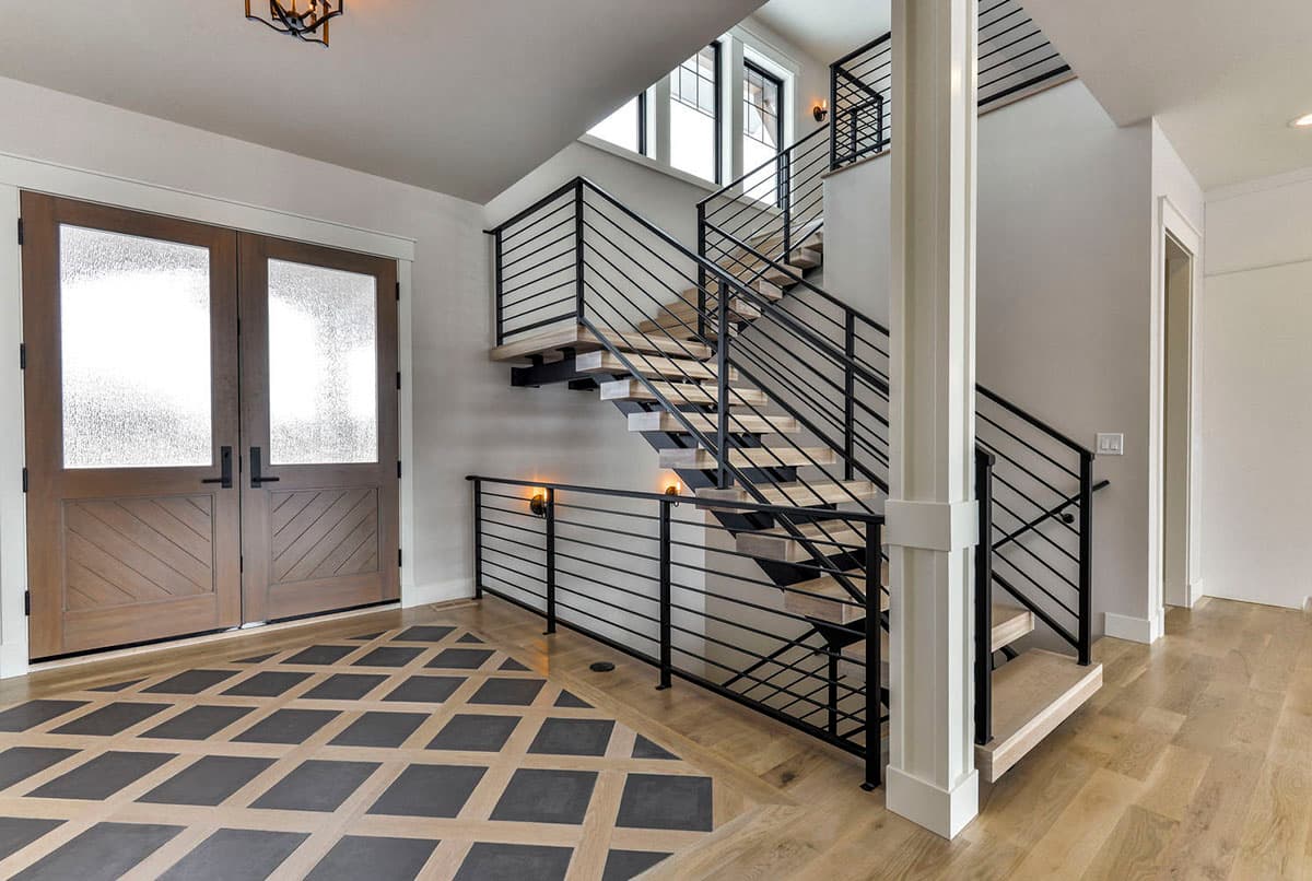 Interior view: Foyer with double wooden doors, open staircase with black metal railing, and patterned flooring.