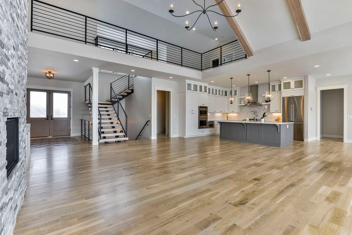 Open concept living space with gray island kitchen, floating staircase, lofted balcony, and stone fireplace.