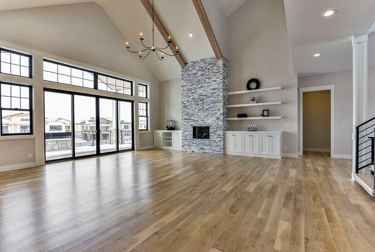 Interior view of great room with vaulted ceiling, stone fireplace, floor-to-ceiling windows, and built-in cabinetry.