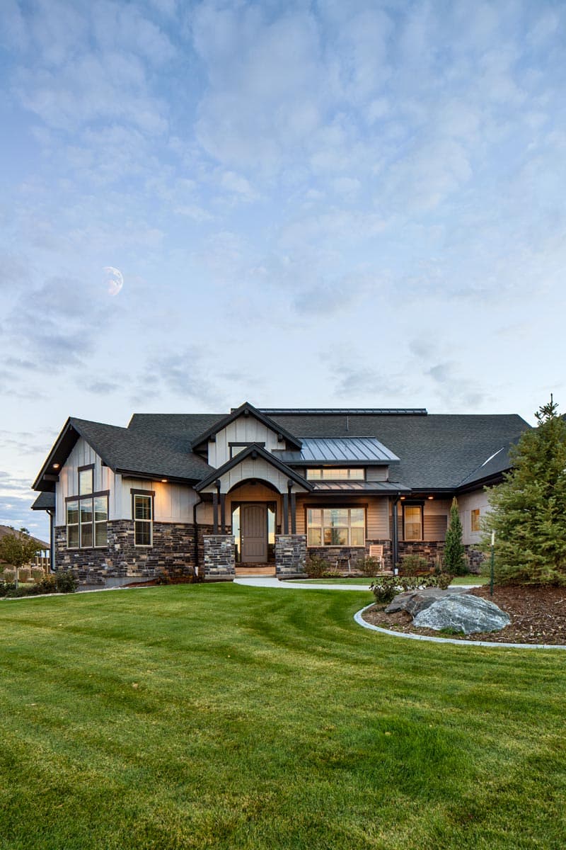 House plan exterior showing a two-story modern farmhouse with stone accents, covered entry porch, and multiple gables.