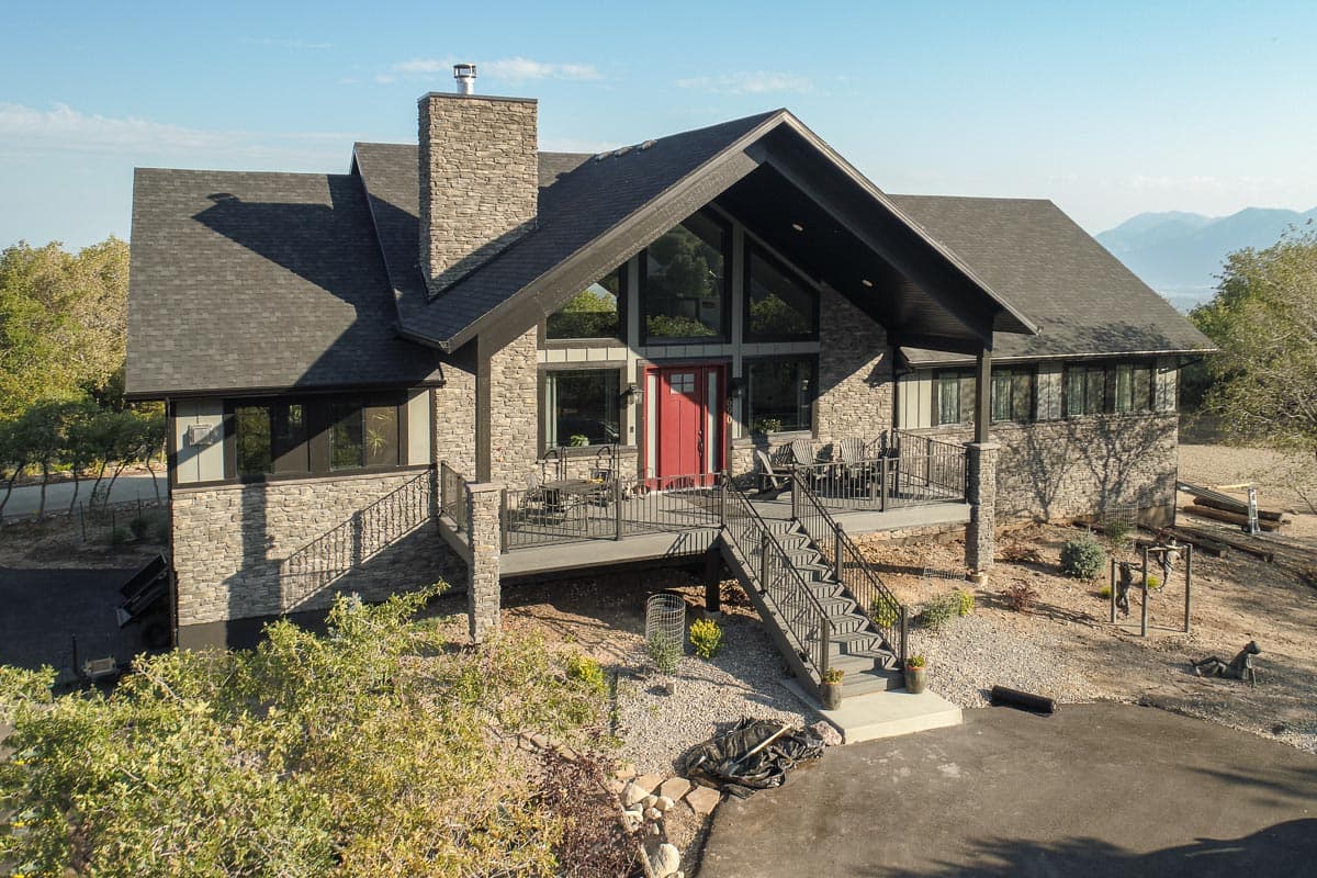 House plan exterior: Modern style with stone and siding, prominent gable roof, large front windows, and a covered deck.