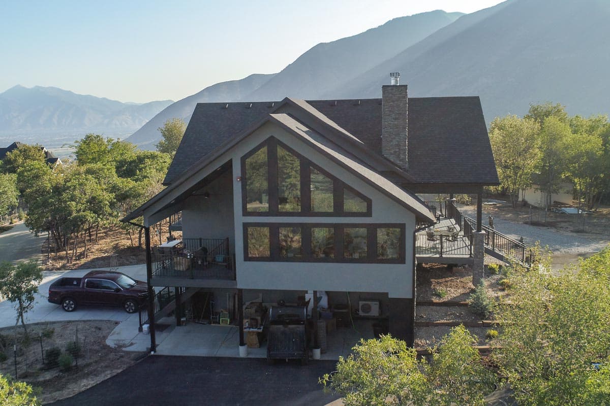 Modern house plan exterior with a steep gable roof, large angular windows, stone chimney, and covered decks.