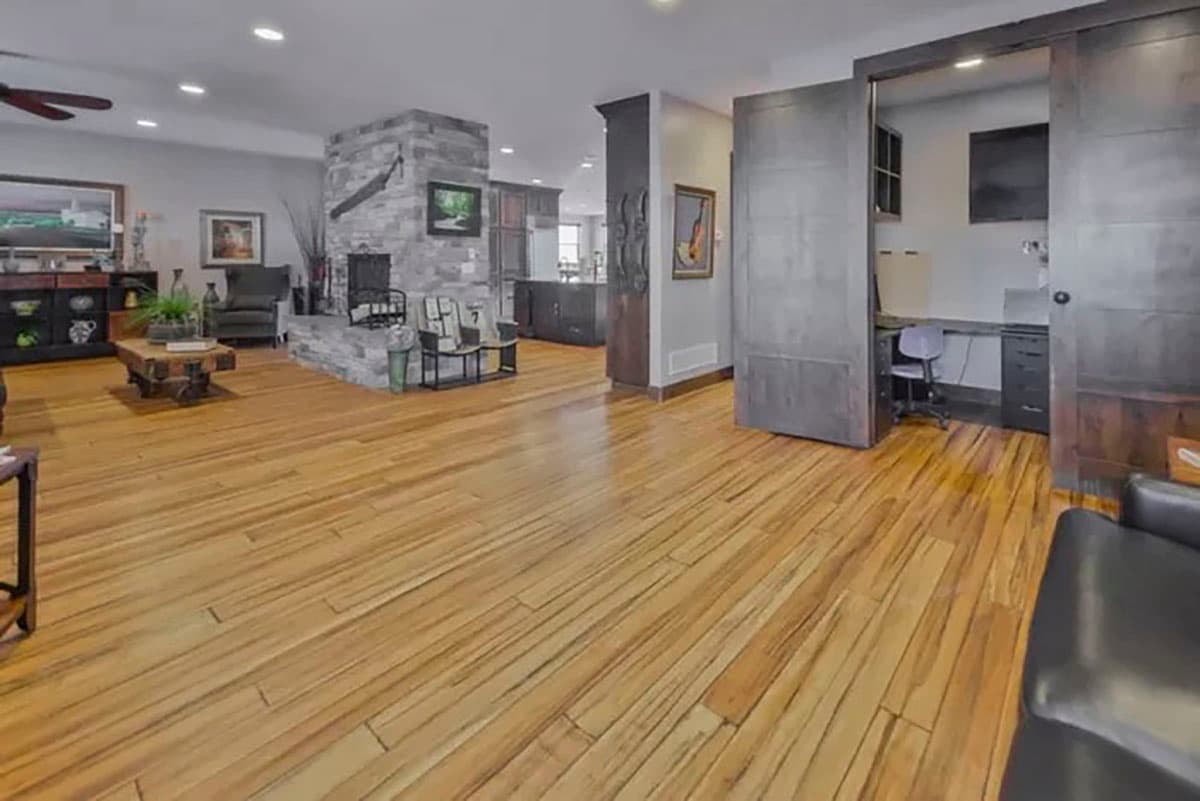Interior view of a living area with a stone fireplace, wood floors, and a sliding door opening to a home office.