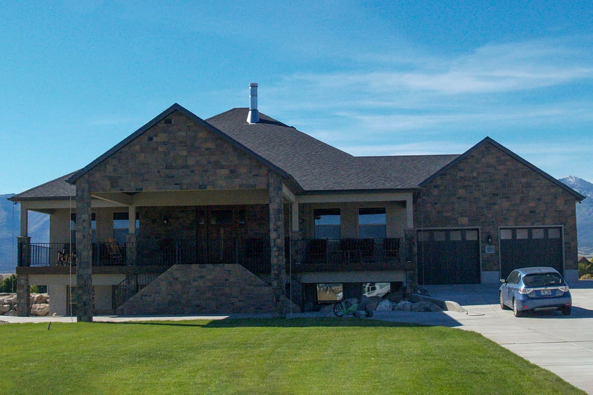 House plan exterior: single-story home with stone facade, covered porch, and attached three-car garage.