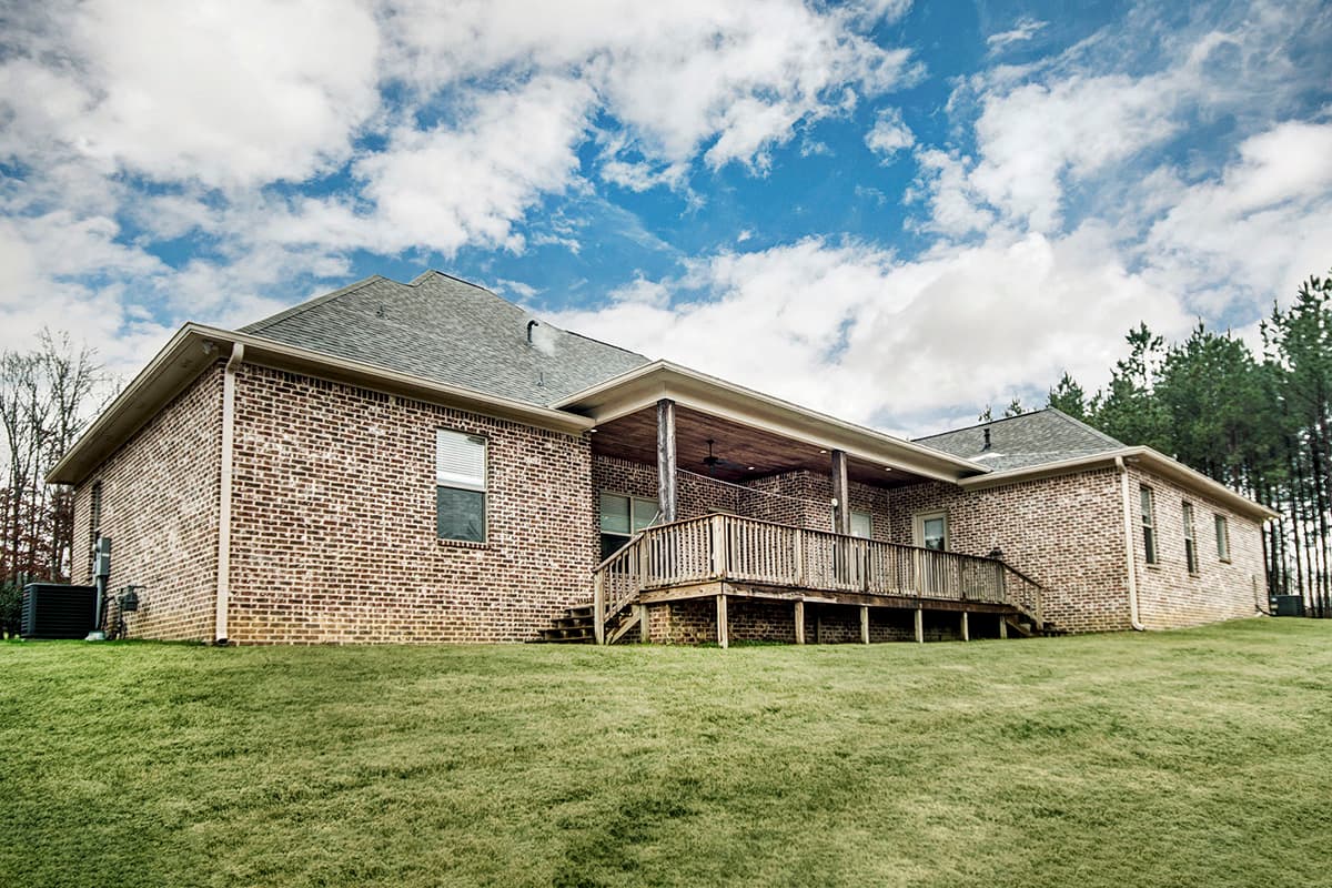 House plan exterior: Brick, two-story home with covered porch, wooden deck, and gable roof.