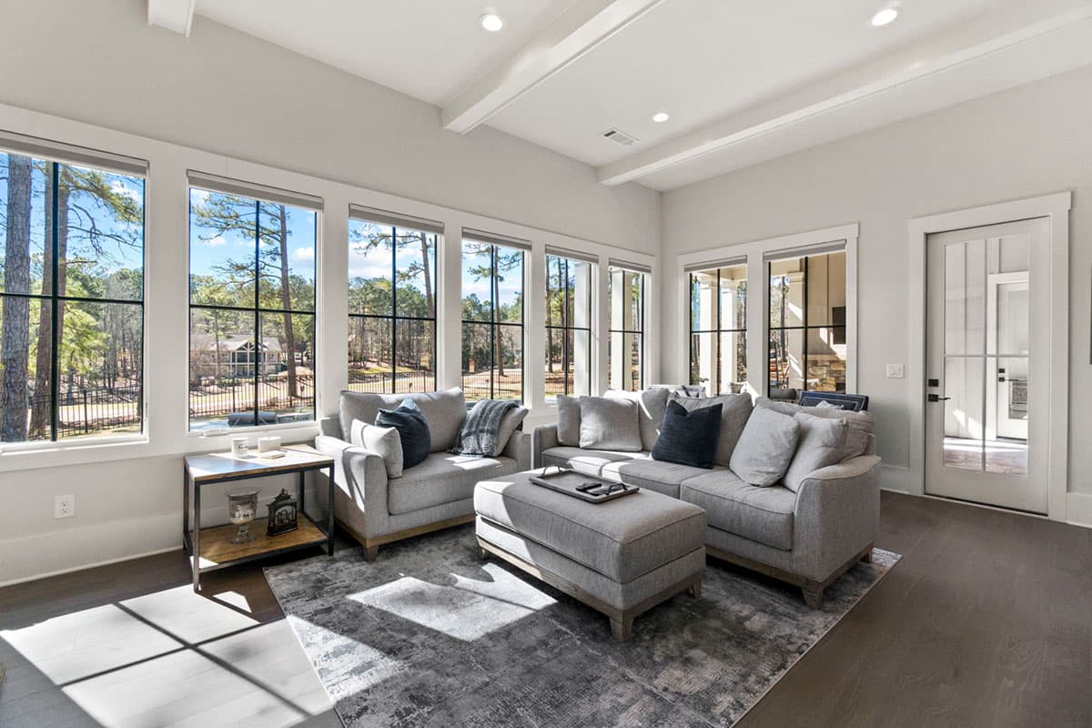 Living room with sofas, ottoman, and patterned rug, featuring a wall of large windows and coffered ceiling.