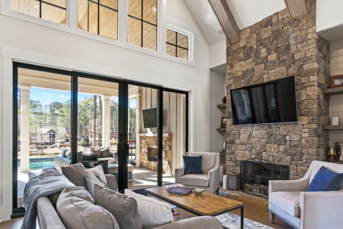 Great room with vaulted wood ceiling, stone fireplace, and large sliding glass doors opening to a patio.