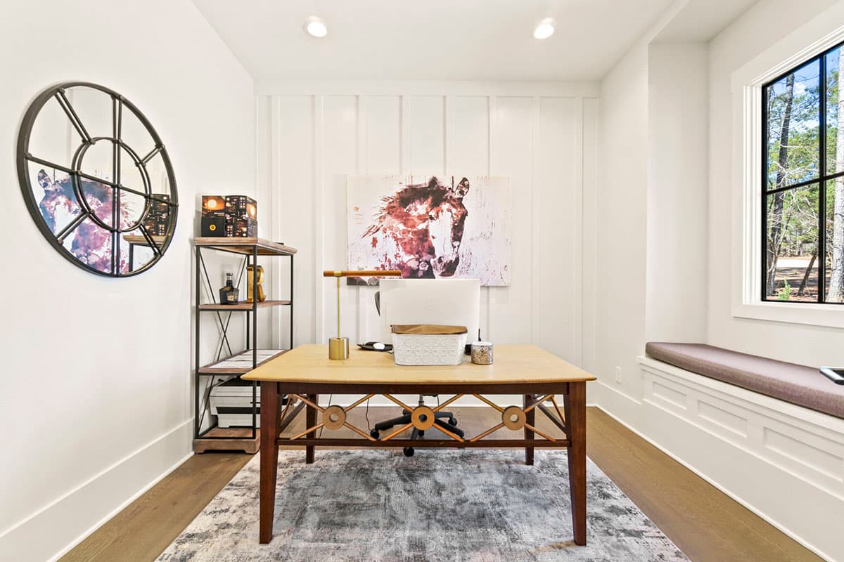 Home office with wooden desk, shelving, art, and window seat.