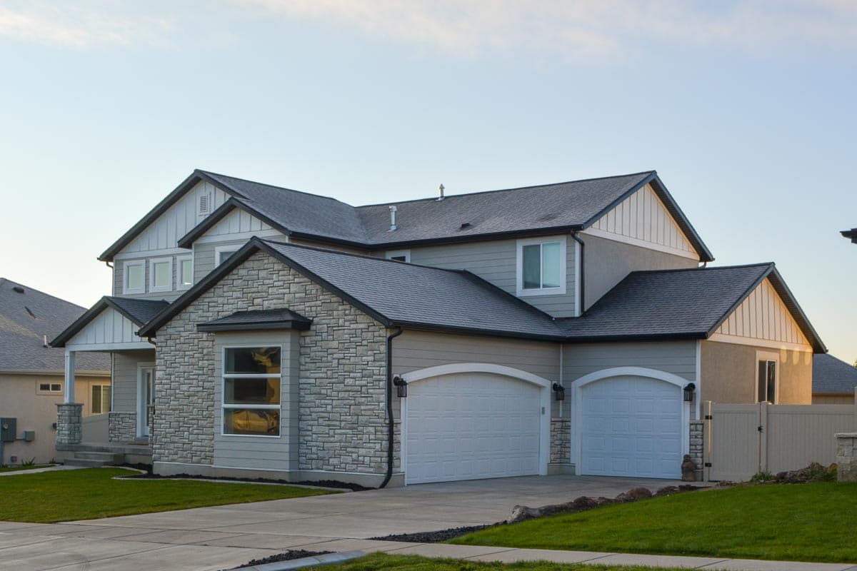 House plan exterior: Two-story home with stone accent facade, prominent gables, and a three-car garage.