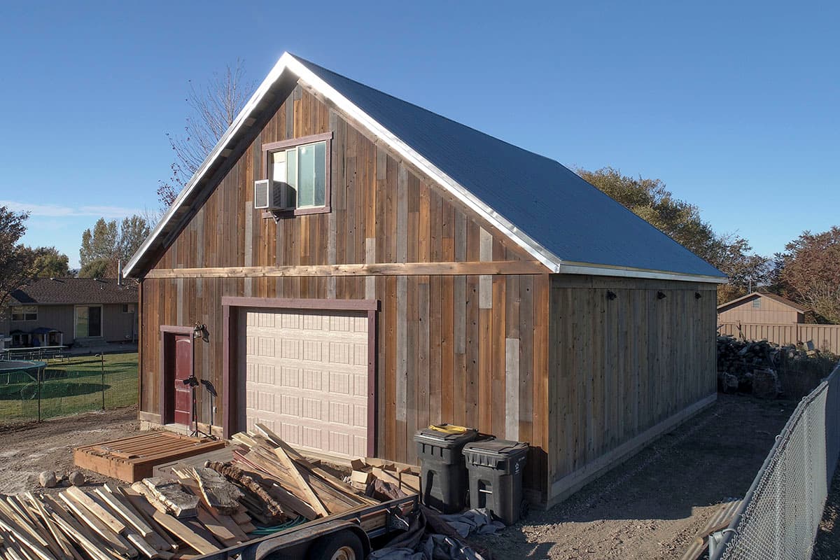 House plan exterior with vertical wood siding, a single garage door, and a metal gable roof.