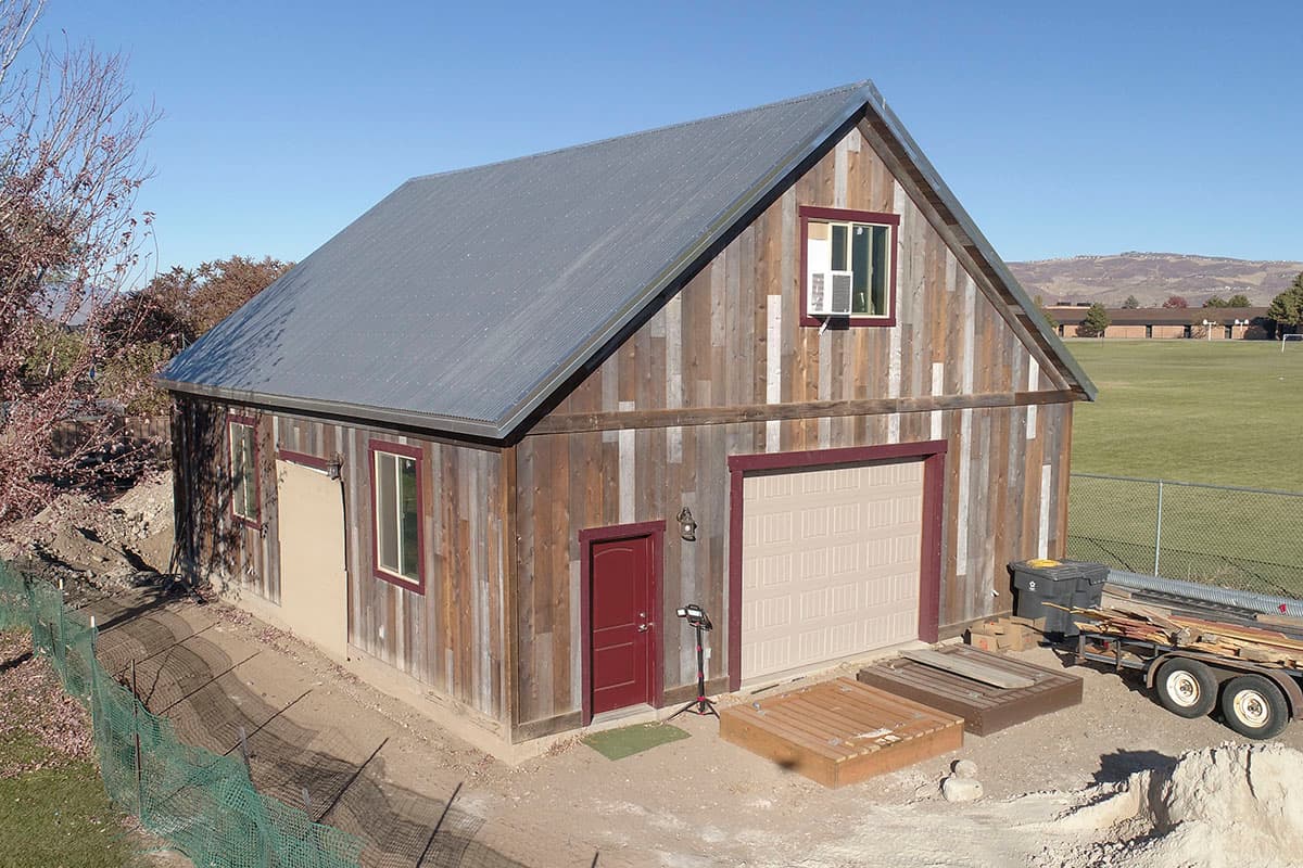 House plan exterior. Two-story barn style building with a metal roof. Features a garage door and gable roof.  Siding is weathered wood planking.