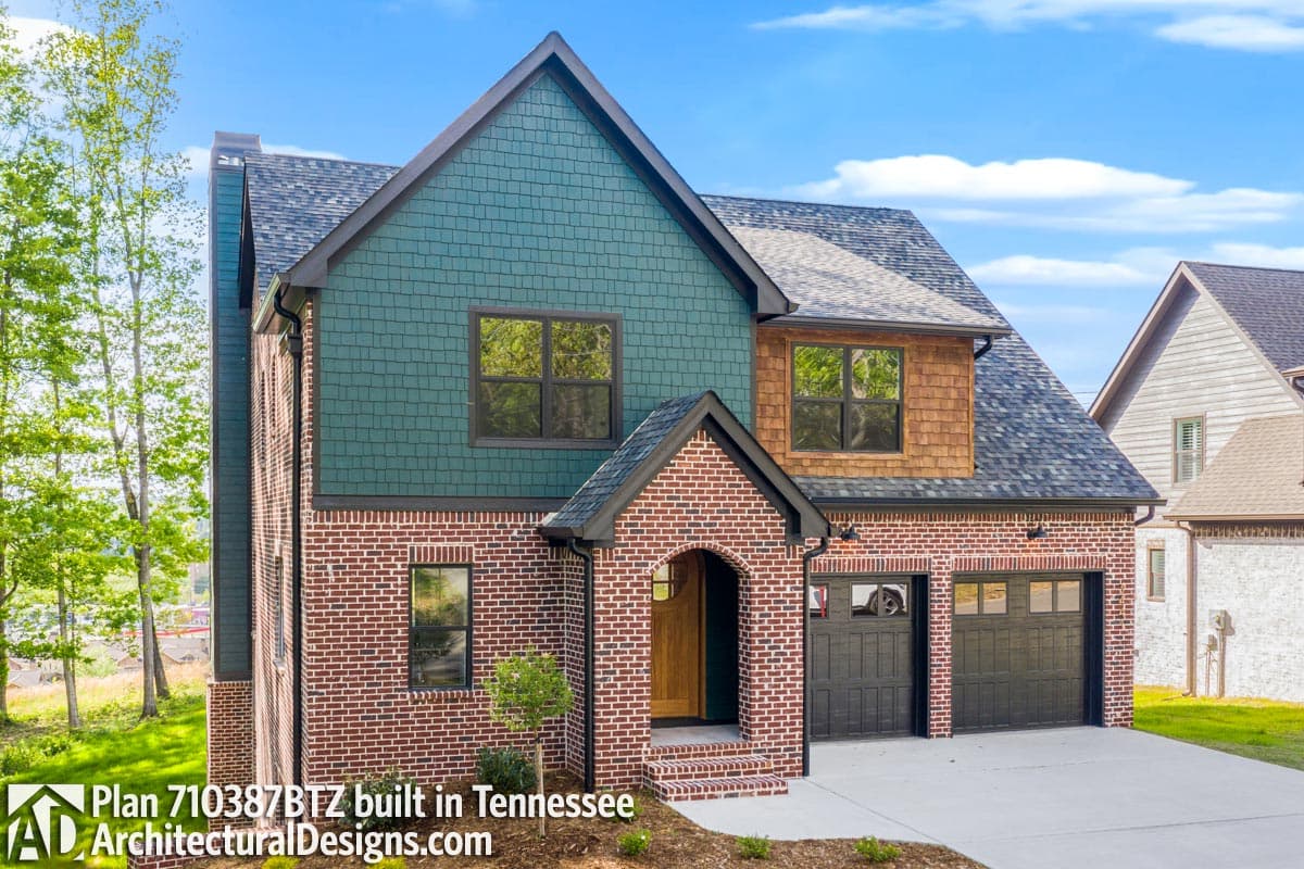 House plan exterior: Two-story home with brick and green shingle siding, arched entry, and a three-car garage.