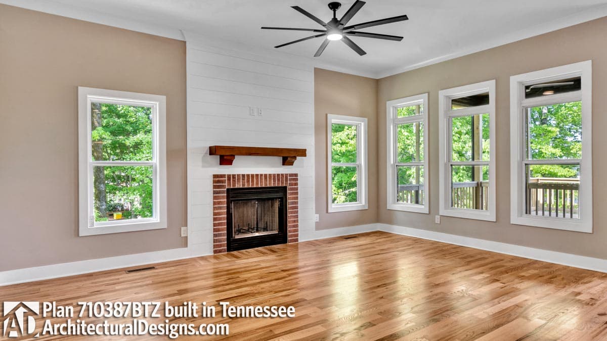Interior view of living room with brick fireplace, shiplap surround, wood mantel, and multiple windows.