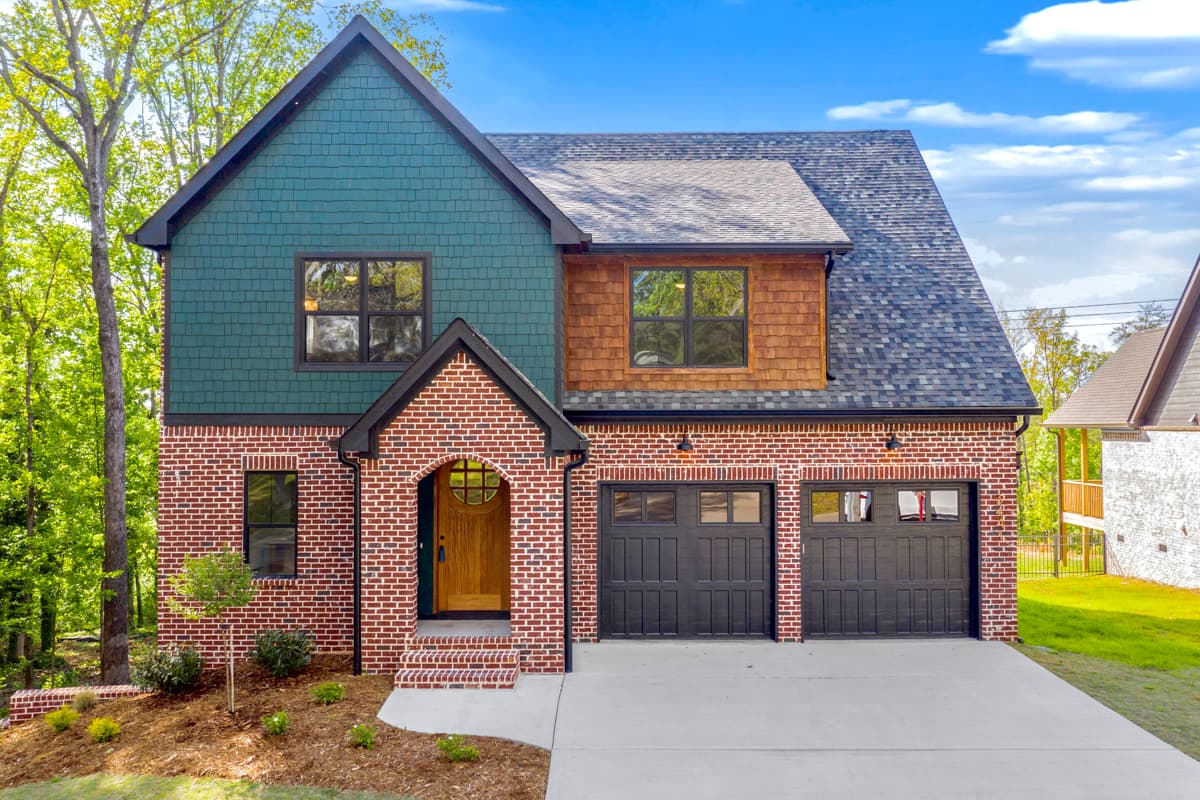 House plan exterior. Two-story brick home with gabled roof, arched entry, and two-car garage. Features include shake siding and contrasting trim.