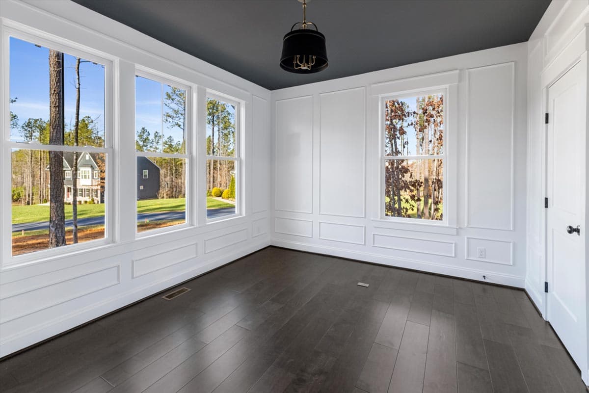 Interior view of a room with large windows, decorative wall molding, and dark hardwood floors.