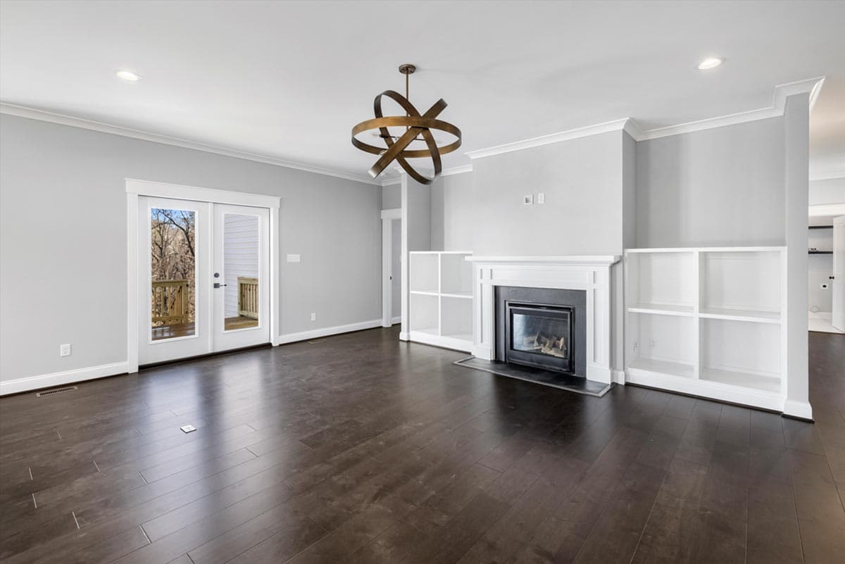 Living room with fireplace, built-in shelving, and double glass doors opening to a deck.