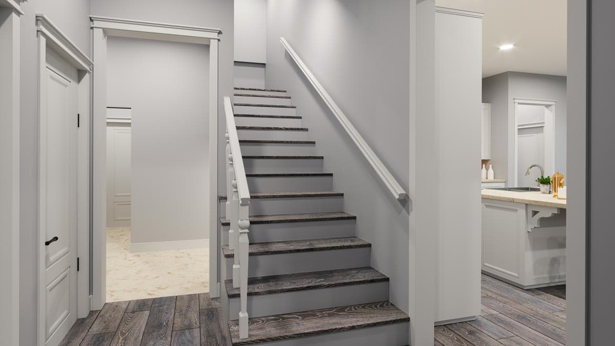 Interior view of a staircase with dark wood treads, white risers and balusters, leading to a kitchen with a light gray island.