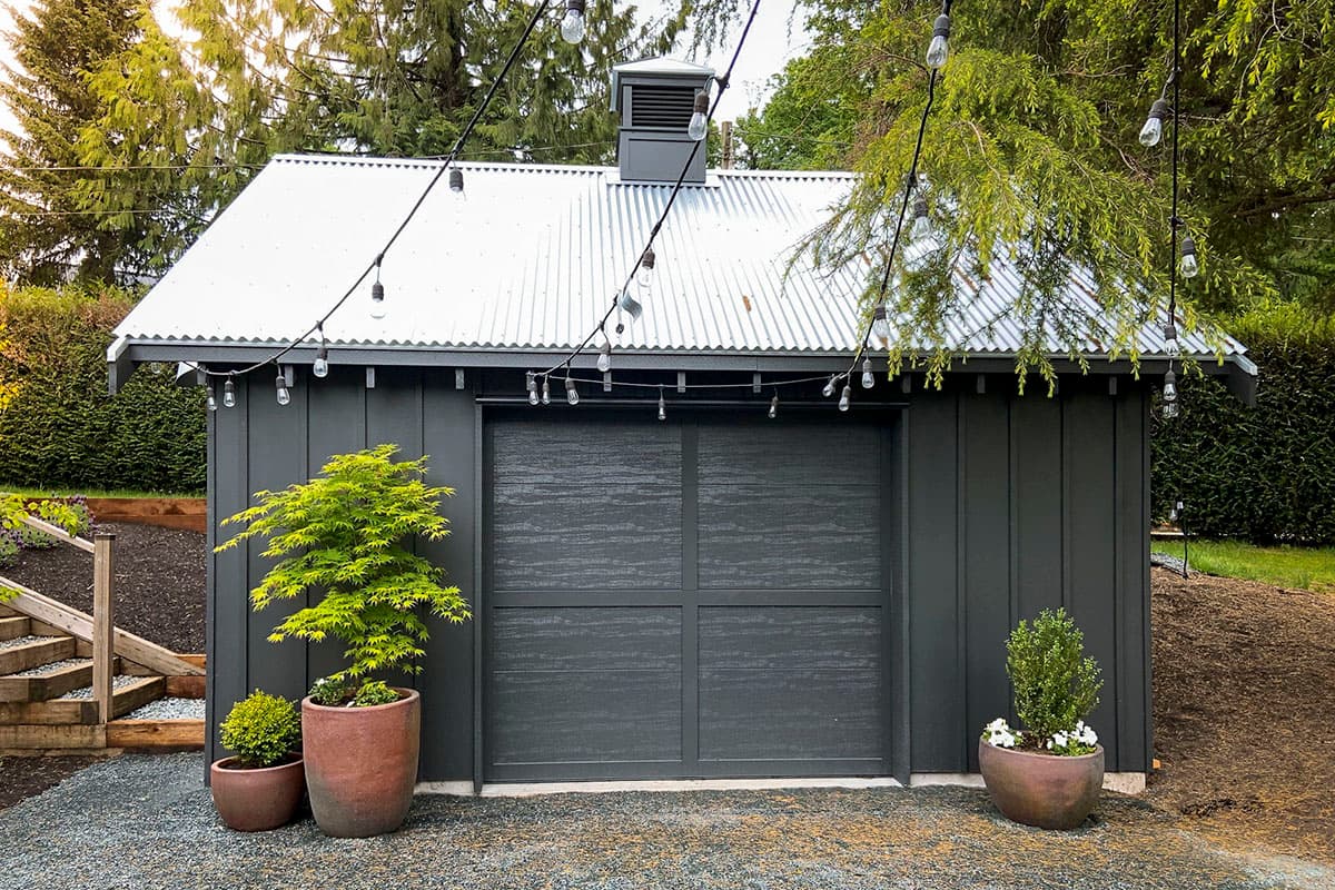 Modern garage exterior with dark vertical siding, corrugated metal roof, and large carriage-style garage door.