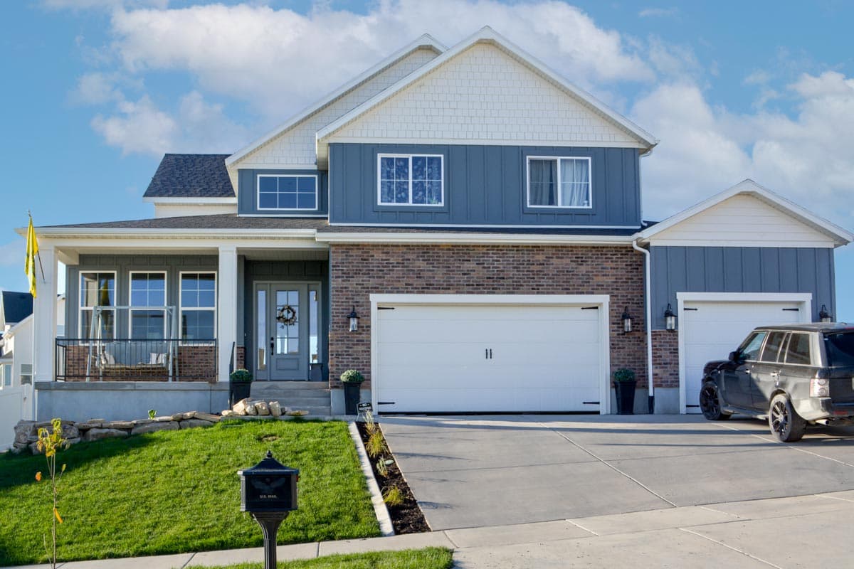 House plan exterior with two stories, covered porch, brick and vertical siding, and a three-car garage.