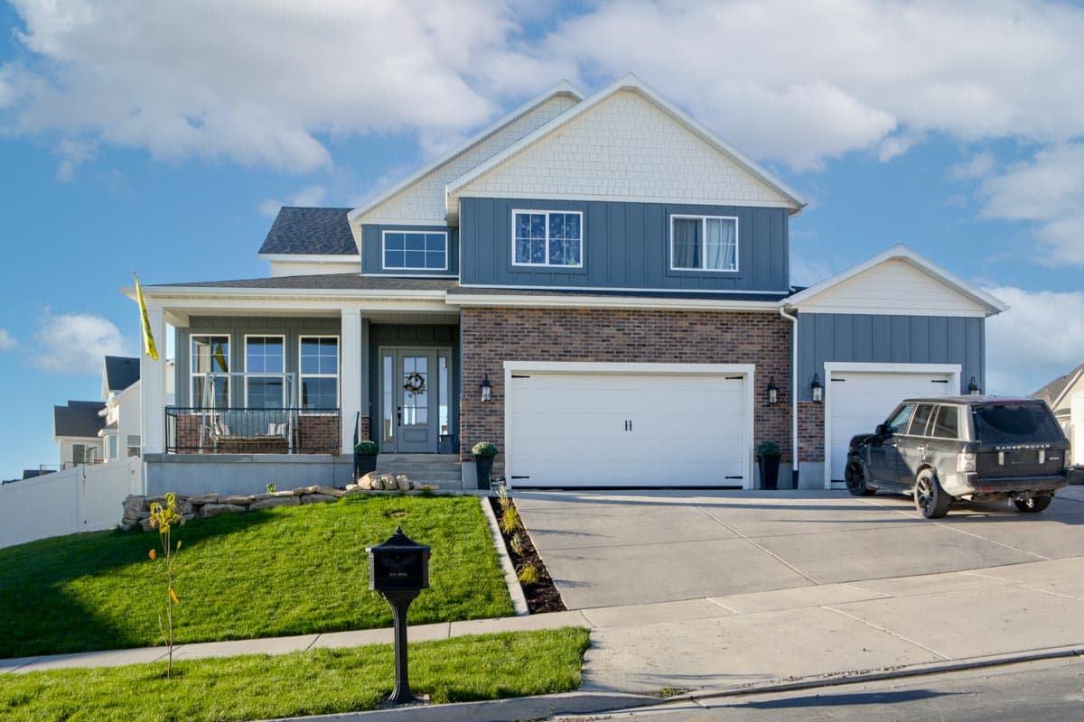 Two-story Modern Farmhouse exterior with gabled roof, covered porch, brick and vertical siding, and a three-car garage.
