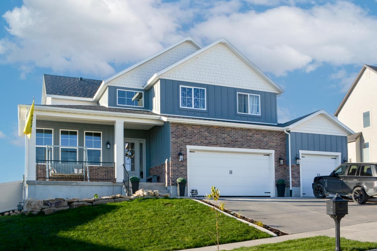 Two-story house plan exterior with a covered porch, blue siding, brick accents, and a three-car garage.
