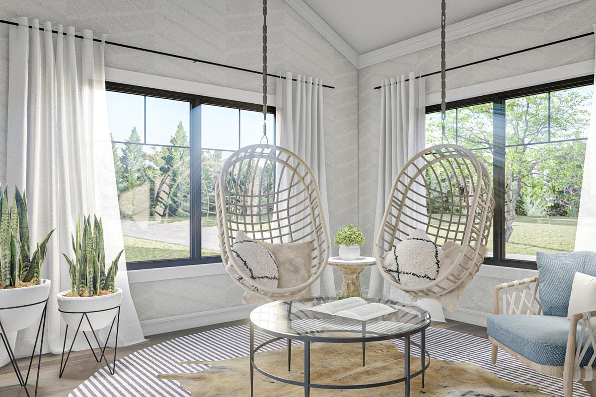 Living area with two hanging chairs, a glass coffee table, and large windows overlooking a yard.