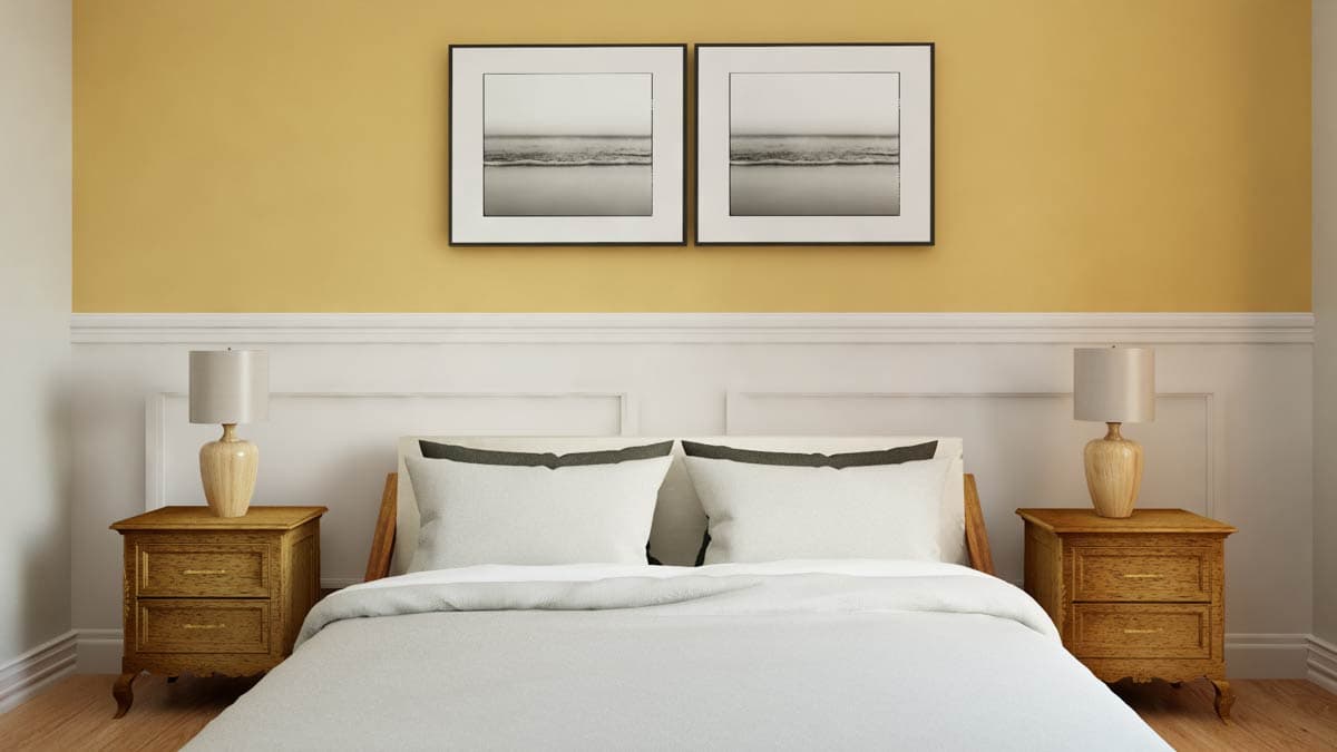 Bedroom interior with a queen bed, two nightstands, and two framed seascape prints above paneled wainscoting.
