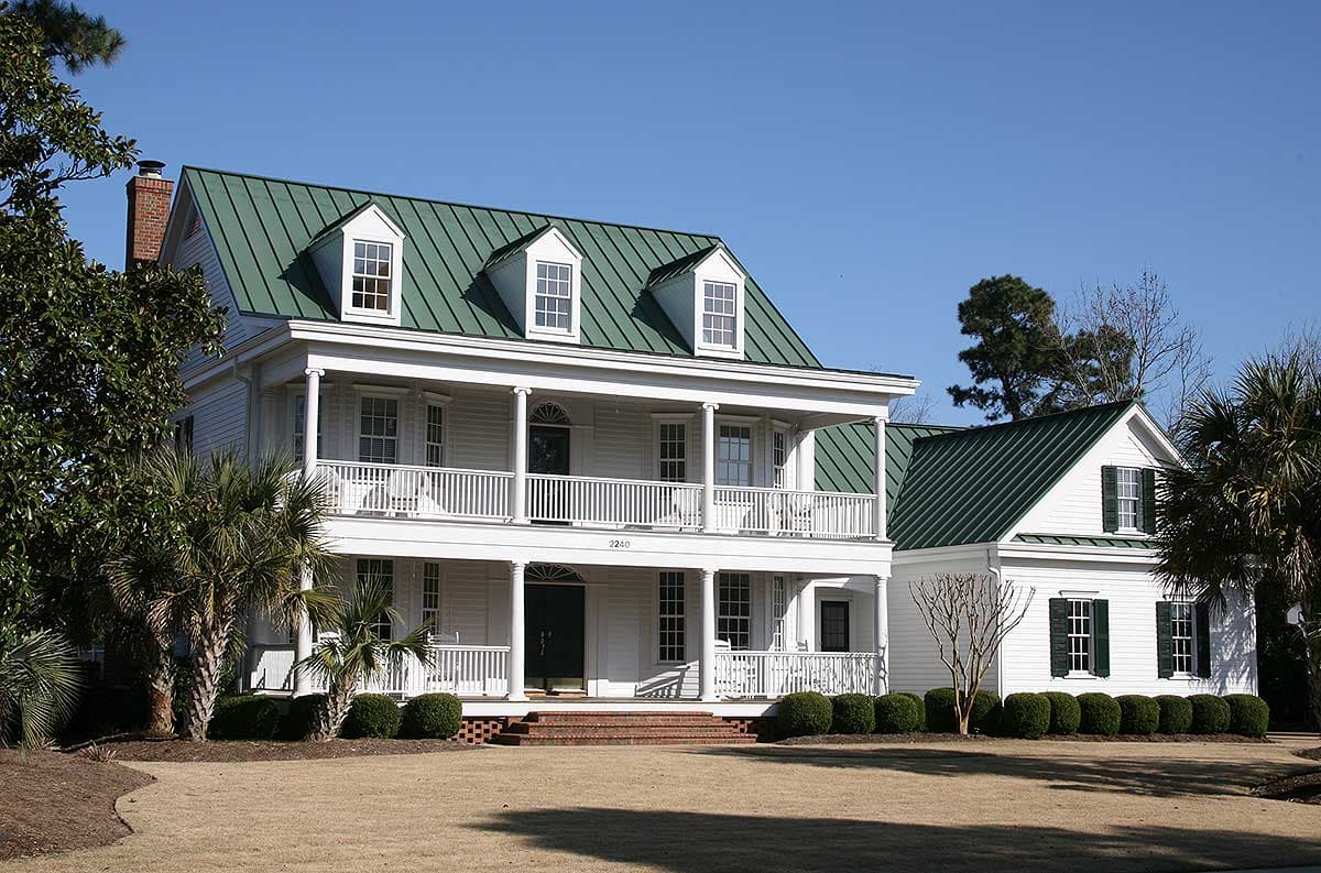 Two-story house plan exterior with a wraparound porch, gables, dormers, and green metal roof.