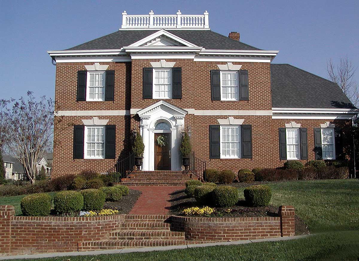 House plan exterior of a two-story brick home with black shutters, prominent pedimented entrance, and rooftop balustrade.