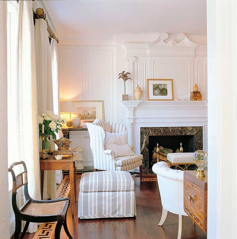 Living room with fireplace, wingback chair, ottoman, and ornate mantelpiece.
