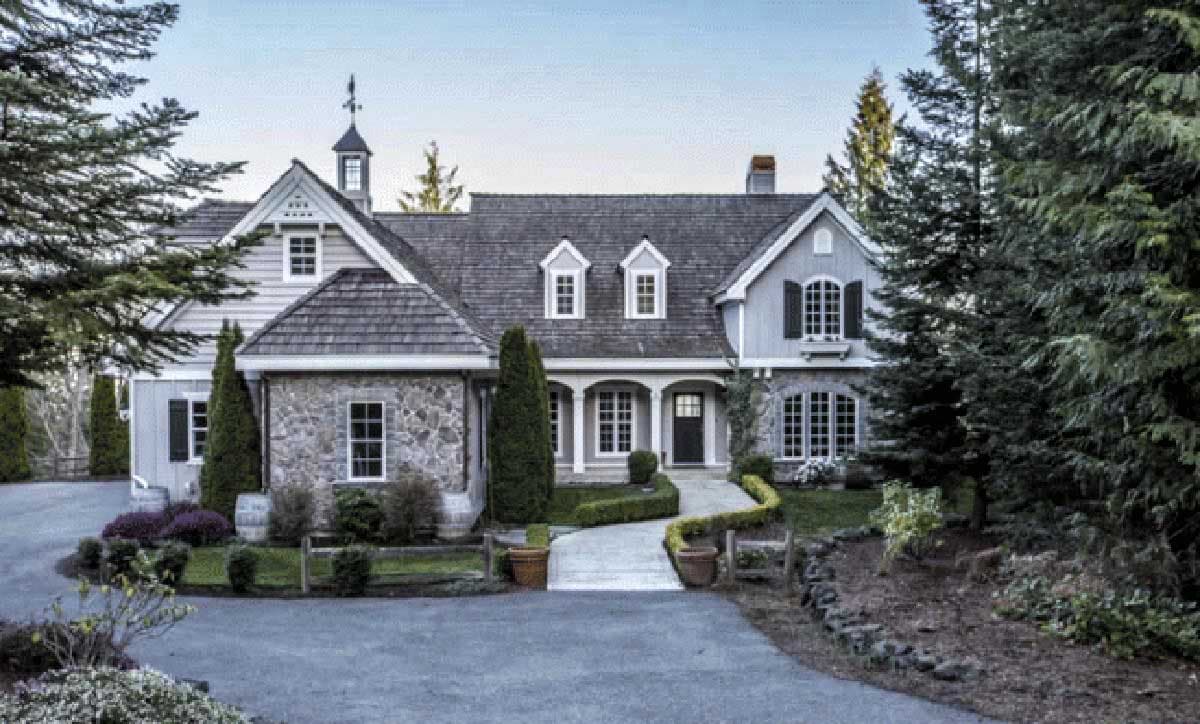 House plan exterior: Stone and shingle siding, multiple gables, arched dormers, and a central covered portico with arched openings.