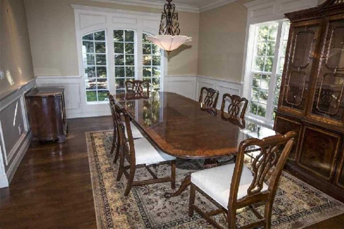 Formal dining room with large oval table, upholstered chairs, bay window, chandelier, buffet, and china cabinet.