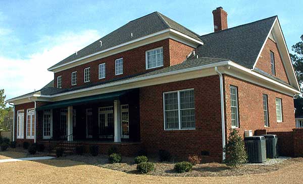 House plan exterior: Two-story brick building with a covered front porch, multiple gables, and a prominent brick chimney.