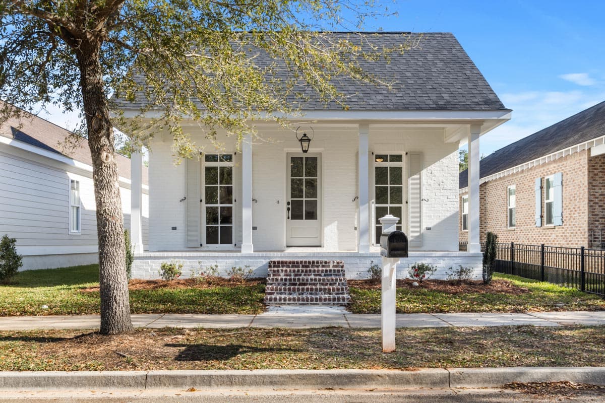 House plan exterior. One-story house with a front porch, columns, and a brick staircase. Features include a gabled roof and shuttered windows.