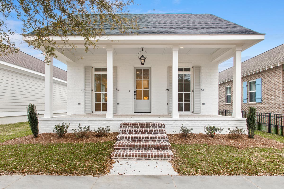 House plan exterior: One-story modern cottage with a covered front porch, brick steps, shutters, and paneled door.