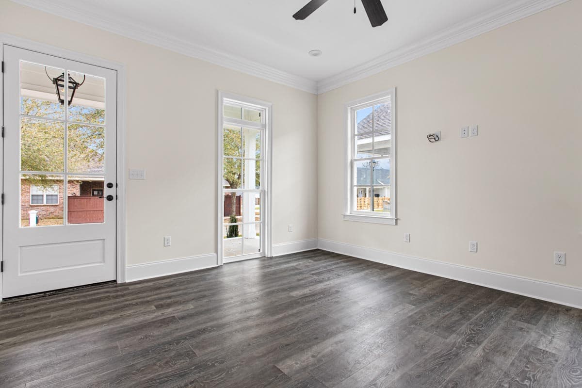 Interior view of a room with French doors, two windows, and dark wood-look flooring.