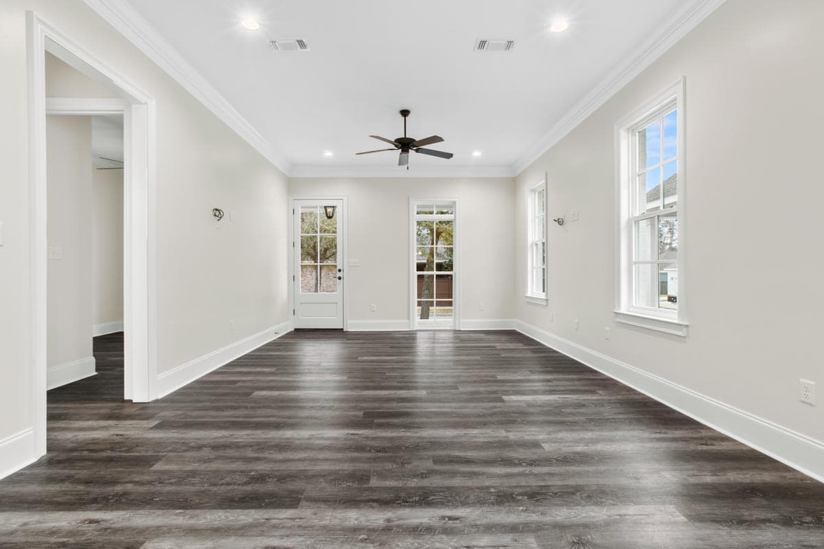 Interior view of a room with white walls, a ceiling fan, a door, large windows, and dark wood-look flooring.