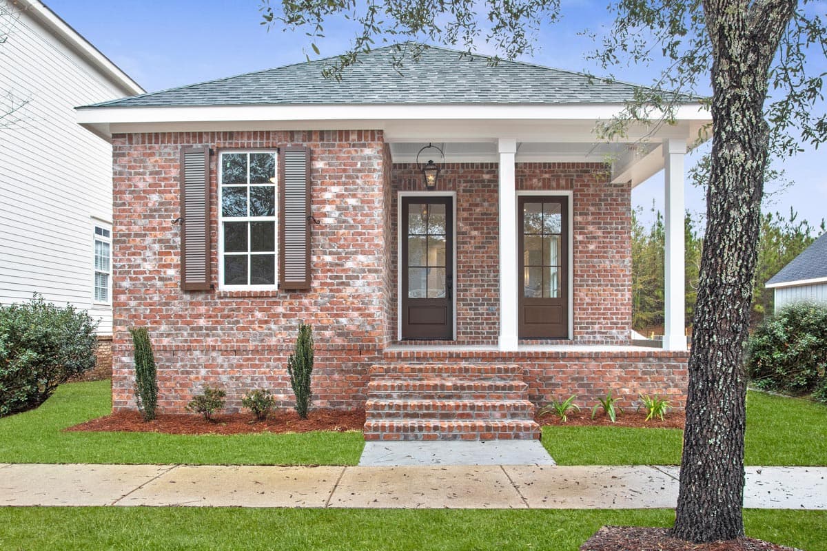 House plan exterior. Single-story brick cottage with a front porch, gabled roof, and two front doors.