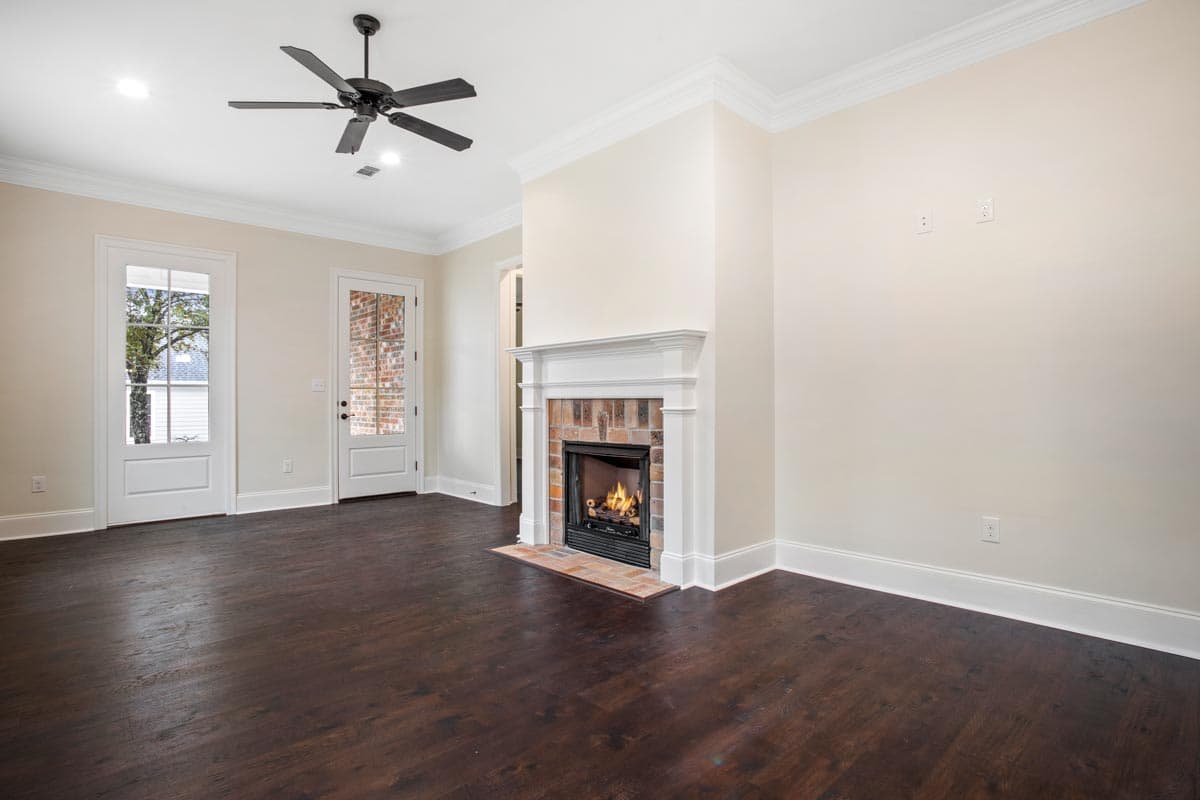 Interior rendering of a living room with a brick fireplace, dark wood floors, a ceiling fan, and two glass-paneled doors.