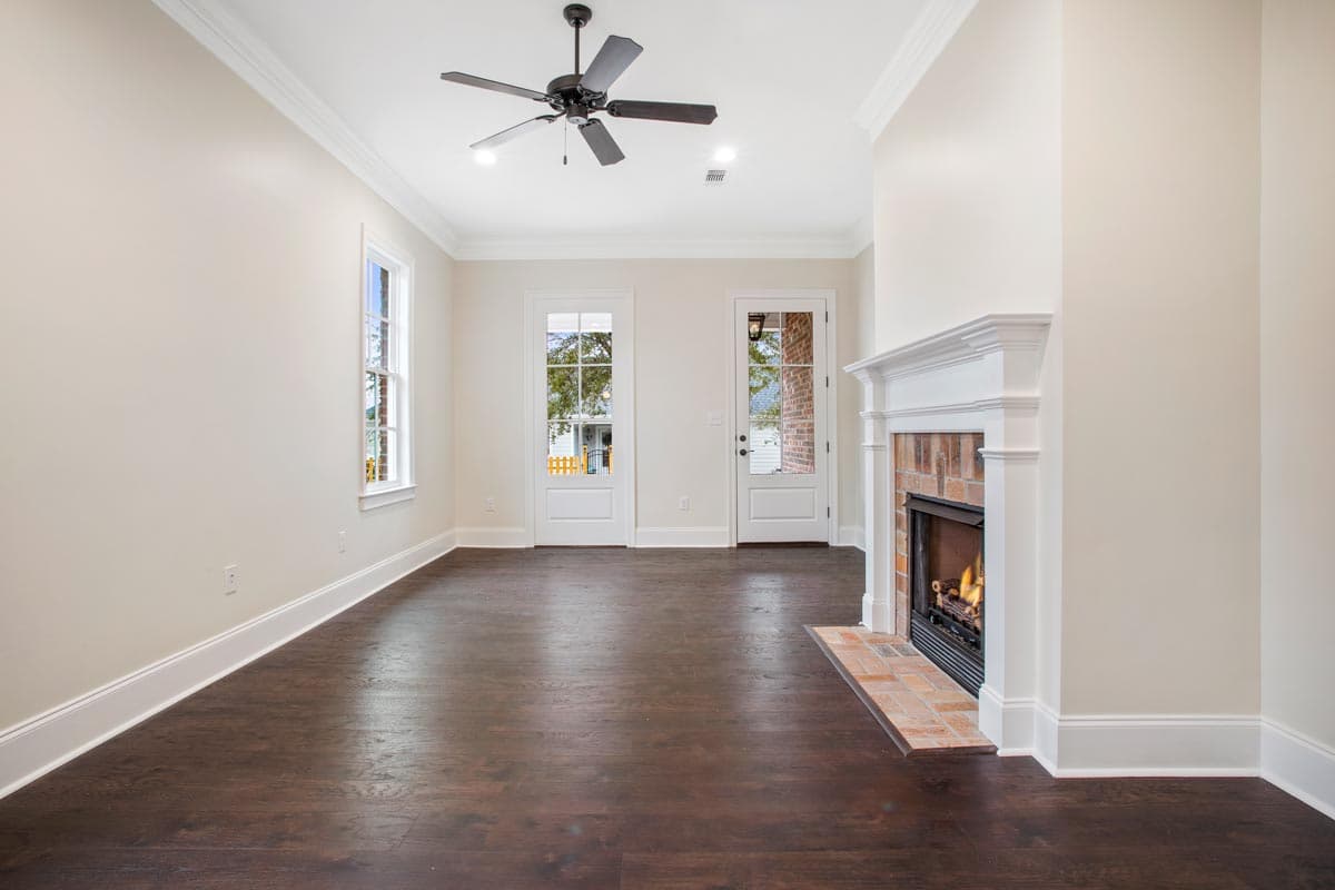 Interior view: living room with fireplace, ceiling fan, and two French doors leading outside.
