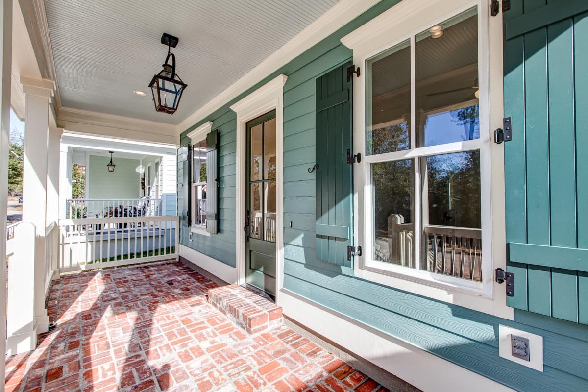 House plan exterior with covered porch, brick patio, decorative door, and louvered shutters.