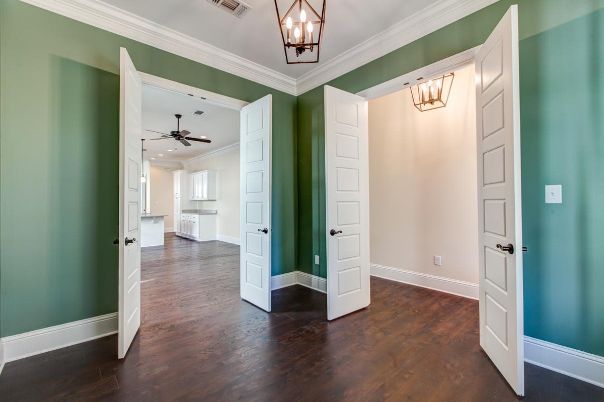 Interior view of a house plan showing a hallway with double doors leading to a kitchen with white cabinets and island.