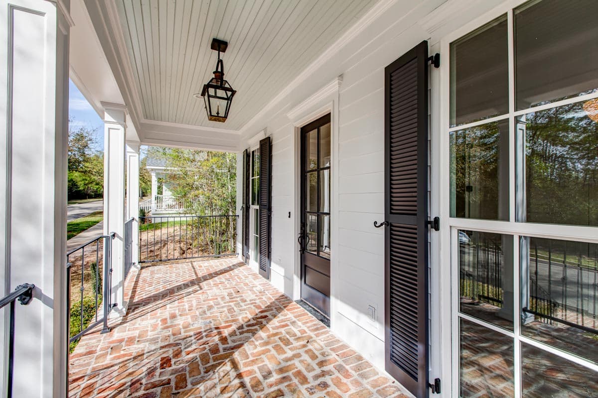 House plan exterior featuring a brick-paved covered porch with columns, black shutters, and a gas lantern.