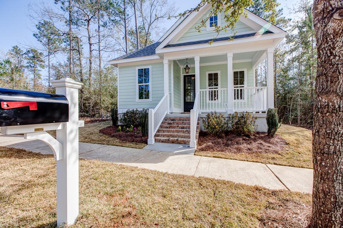 House plan exterior: Two-story cottage with a covered front porch, white railings, and multiple gables.
